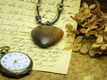 Brief, auf dem sich eine Kette mit einem Medaillon in Herzform und eine Taschenuhr befinden, rechts daneben liegen Zweige mit verwelkten Blättern