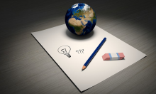 ein weißes Blatt Papier, ein Radiergummi, ein Bleistift und ein Globus; auf dem Blatt Papier sind eine Glühbirne und 3 Fragezeichen gezeichnet
