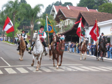 Umzug mit Personen in Tiroler Tracht auf Pferden, im Hintergrund Palmen