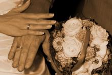 2 Hände mit Hochzeitsringen übereinanderliegend, daneben ein Hochzeitsstrauß