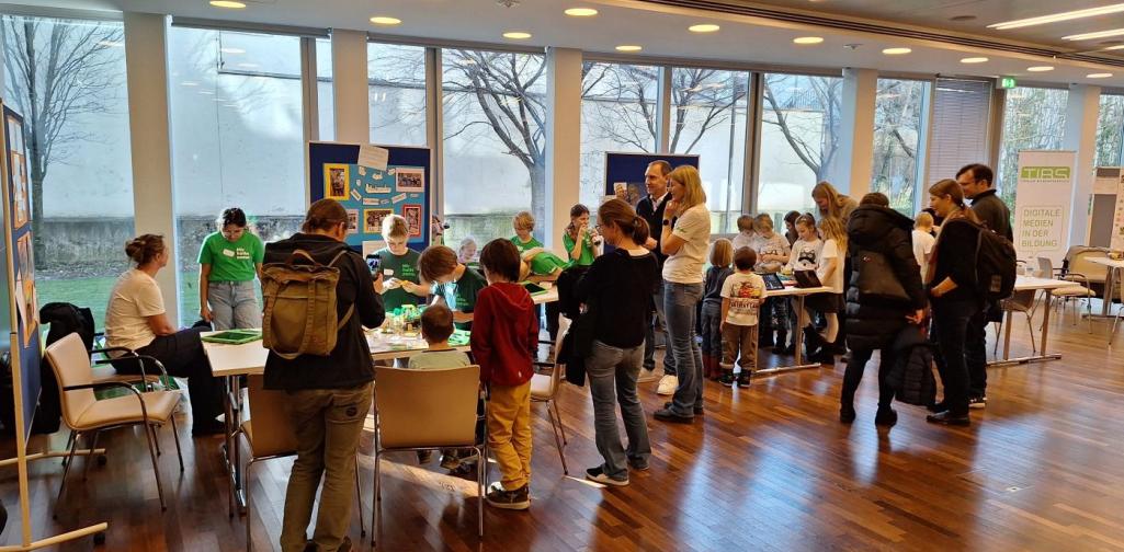 Kinder und Interessierte stehen um den Modelltisch. Im Hintergrund sieht man die Plakate zu den Modellen.